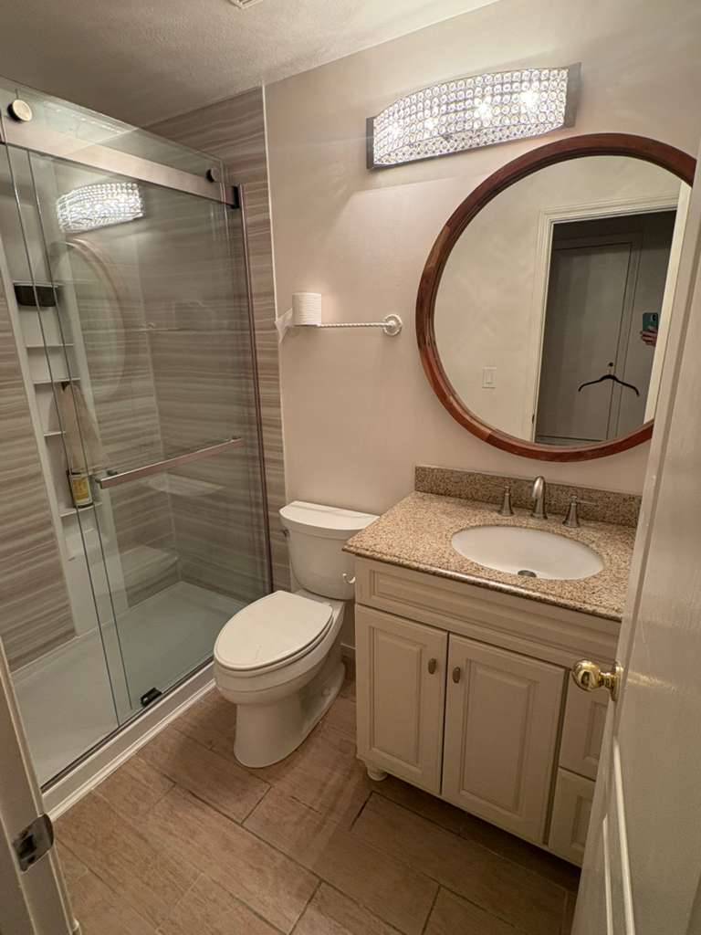 After — finished bathroom with glass shower, granite vanity and crystal lighting