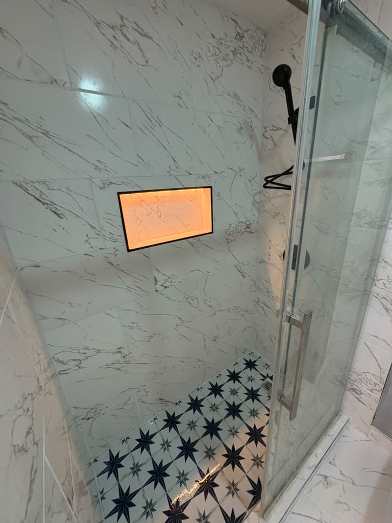 Finished marble-look shower with lighted niche, star-pattern tile floor and glass door in Las Vegas