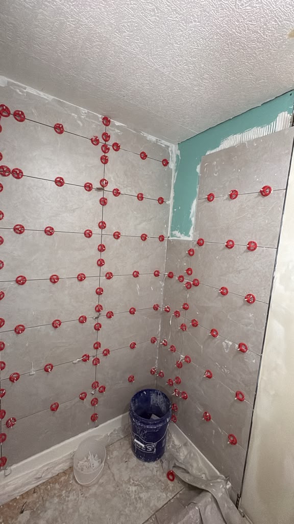 Large-format grey shower tile going up with red leveling clips in a Las Vegas bathroom remodel